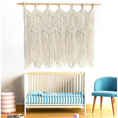 Un rideau en macramé de couleur crème est suspendu à une tringle en bois au-dessus d'un lit de bébé en bois clair avec des draps bleus. À gauche du lit, un panier rond en osier avec des rayures roses et crème repose sur le sol en bois clair. À droite, une petite chaise d'appoint rembourrée en tissu bleu clair avec des pieds en bois complète l'aménagement de la chambre au mur blanc.