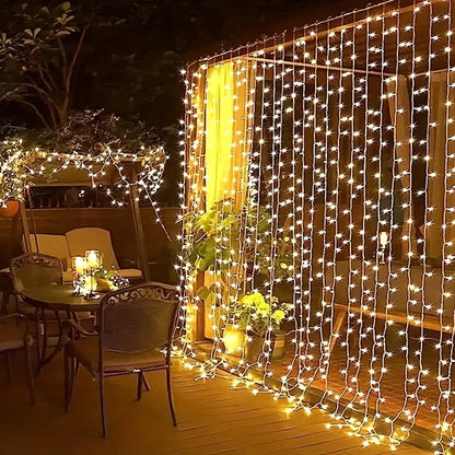Une table et des chaises installées sur une terrasse en bois sont entourées de guirlandes lumineuses suspendues à une pergola. Une petite plante en pot est posée à proximité, doucement éclairée par Guirlande solaire extérieur-rideau | Lumière heureuse, créant une atmosphère accueillante et sereine.