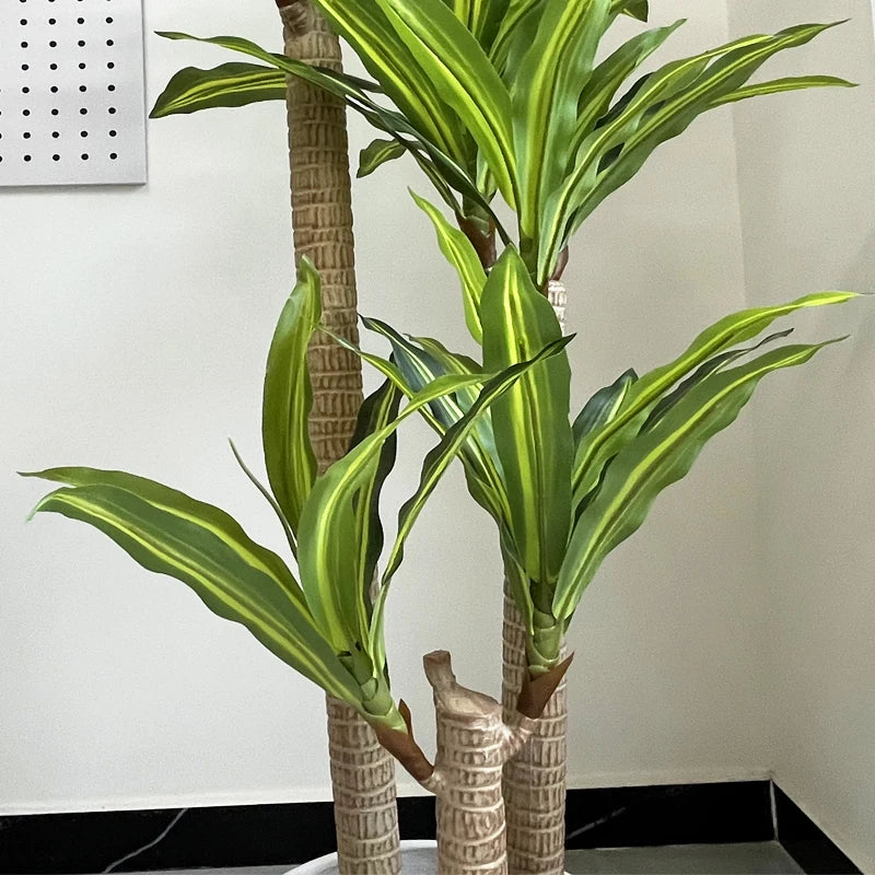 Gros plan de la Plante artificielle d'intérieur-Dracaena, dotée de hautes tiges texturées et de longues feuilles vertes à rayures jaunes, idéales pour décorer n'importe quel espace de vie contre un mur blanc.