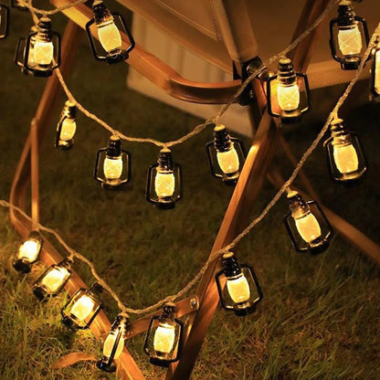 GUIRLANDE EXTERIUR SOLAIRE | Lumière Heureuse Des guirlandes lumineuses sont suspendues à une chaise en bois et projettent une lumière jaune chaude sur la pelouse. Cela crée un cadre chaleureux, idéal pour un arrangement lumineux de camping en plein air ou comme décoration de Noël lors de rassemblements dans le jardin.
