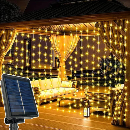 Un belvédère décoré de guirlandes solaires extérieures-rideaux « Lumière heureuse » crée une ambiance chaleureuse. À l'intérieur se trouve un coin salon avec un canapé et des chaises, tandis qu'un panneau solaire au premier plan indique que les lumières sont alimentées par l'énergie solaire, fermant partiellement l'espace.