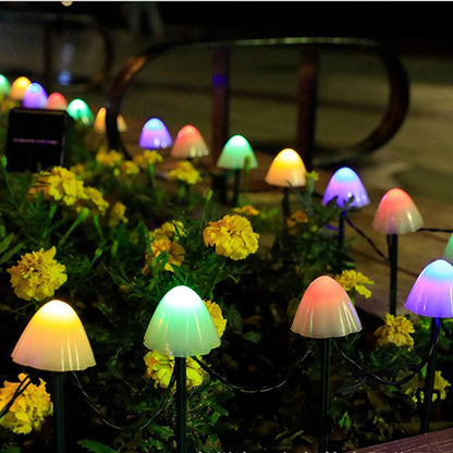 Des lumières en forme de champignon brillent parmi les fleurs jaunes d'un jardin la nuit, alimentées par Nuit Lumineuse Guirlandes solaire extérieur-champignon, créant une atmosphère fantaisiste.