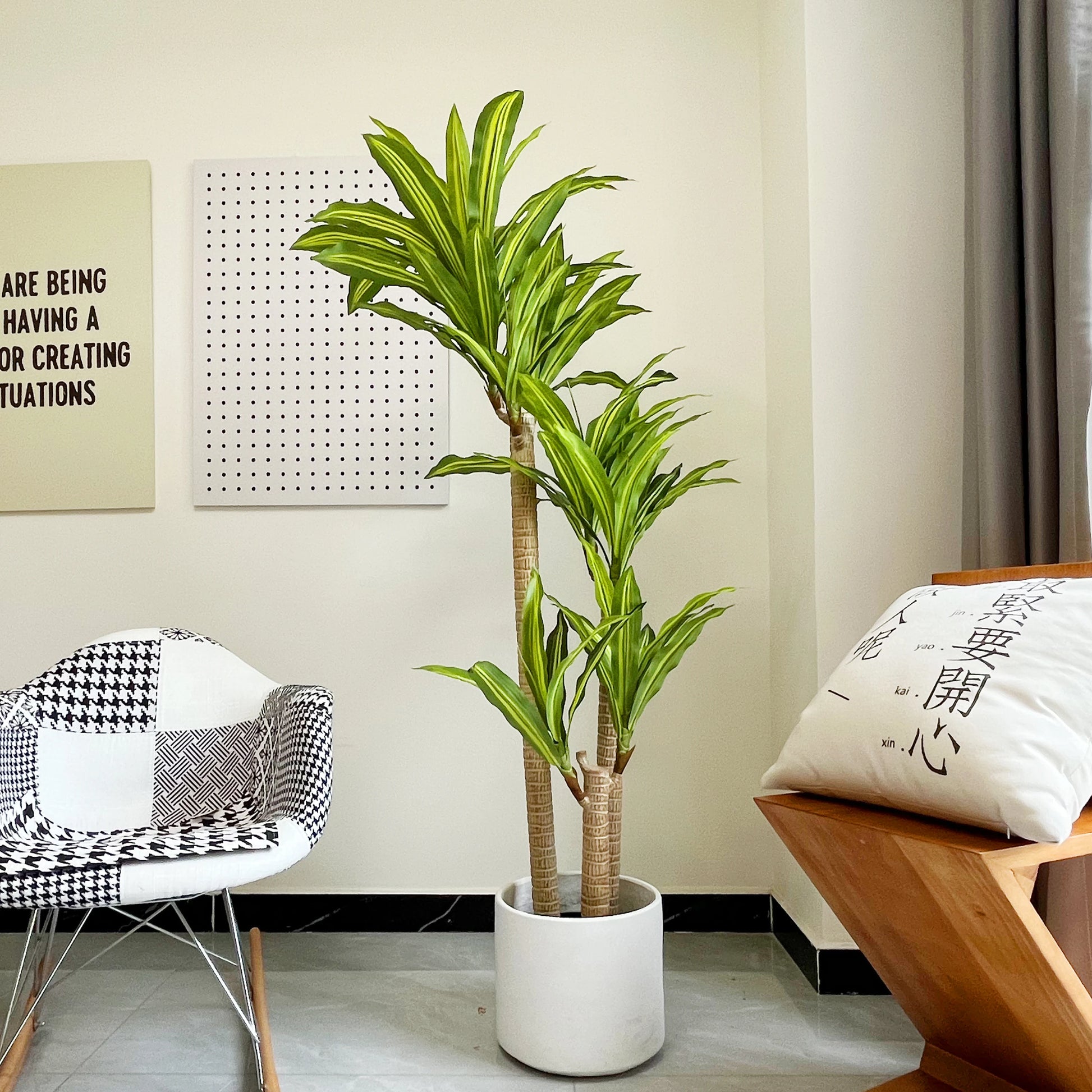 Une plante artificielle d'intérieur-Dracaena aux feuilles rayées vertes et jaunes se dresse sur le sol d'une pièce moderne avec des murs clairs, une chaise à motifs, une chaise en bois avec un coussin imprimé et un décor élégant qui rehausse votre espace de vie.
