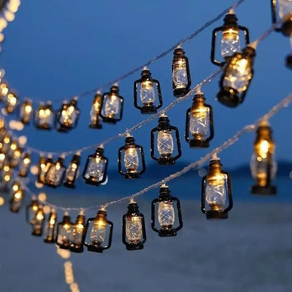 Sous un ciel crépusculaire, les guirlandes GUIRLANDE EXTERIUR SOLAIRE | Lumière Heureuse brillent chaleureusement telles des lanternes vintage. Leur lumière douce et leur silhouette créent une atmosphère chaleureuse et conviviale rappelant les décorations de Noël.