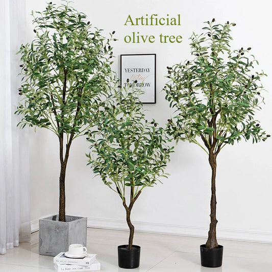 Trois oliviers artificiels d'extérieur en pots noirs et gris apportent une touche méditerranéenne à votre espace. Exposez-les à l'intérieur, près d'un mur blanc, avec une œuvre encadrée et l'inscription « Olive artificiel d'extérieur » en vert.