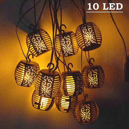 Dix lanternes LED décoratives aux motifs découpés ornés sont suspendues devant un mur, ressemblant à la Guirlande extérieure solaire | Flamme. La lumière jaune chaude crée des ombres complexes et une ambiance chaleureuse et accueillante.