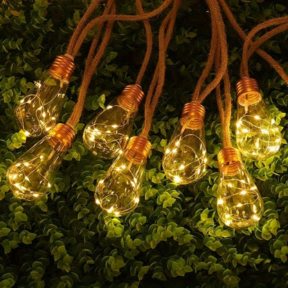 Une guirlande de Guirlandes solaires extérieur | SunGlow aux filaments lumineux est suspendue contre un feuillage vert luxuriant, émettant une lumière dorée chaleureuse et chaleureuse pour une ambiance accueillante.