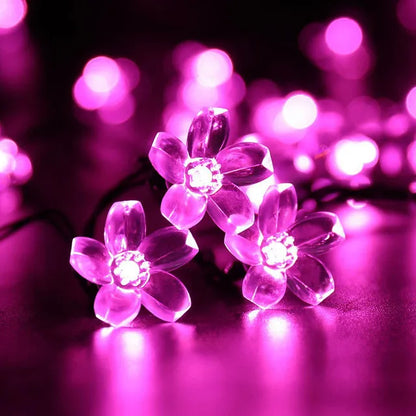 Dans un jardin fantaisiste, des fleurs Rose éclatantes et lumineuses illuminent, tandis que les pétales délicats rayonnent de nuances de rose, projetant une lueur enchanteresse sur le feuillage sombre environnant. Une palissade blanche se dresse majestueusement en arrière-plan, renforçant cette atmosphère sereine et onirique.
