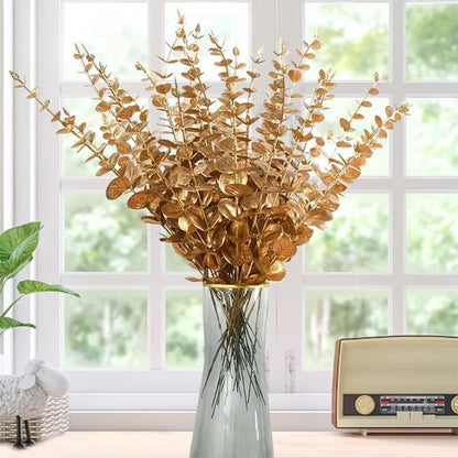 Un vase en verre rempli de Plantes artificielles comme des vraies-Feuilles D'eucalyptus Doré se trouve sur un rebord de fenêtre. Une radio vintage et une verdure réaliste ajoutent du charme, et une grande fenêtre révèle des vues luxuriantes, idéal pour une décoration d'intérieur élégante.