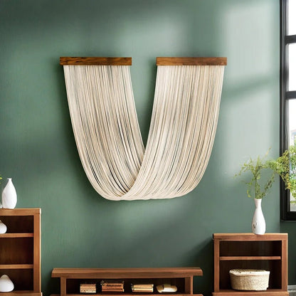 Une décoration murale en macramé beige clair est suspendue à deux supports en bois foncé sur un mur vert olive. Les cordes forment une courbe élégante, apportant une touche artisanale et bohème à l'espace. La texture du macramé crée un contraste subtil avec la surface lisse du mur. Cette pièce de macramé unique est un élément de décoration intérieure artistique.