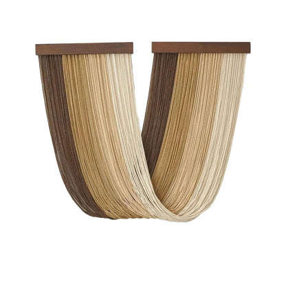 Une décoration murale en macramé présente des cordes beiges et marron clair suspendues à une barre en bois sombre. Les cordes forment un motif ondulé et drapé, créant une texture douce et un aspect artisanal. Cette pièce de macramé apporte une touche bohème et naturelle à un intérieur.
