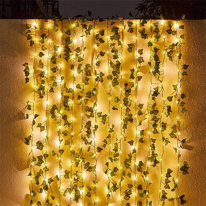 Guirlande lumineuse jaune chaud de la Guirlande solaire extérieure | Lueur de bonheur entrelacé de lierre vert artificiel drapé contre un mur uni, créant une ambiance féerique et une toile de fond lumineuse et décorative.
