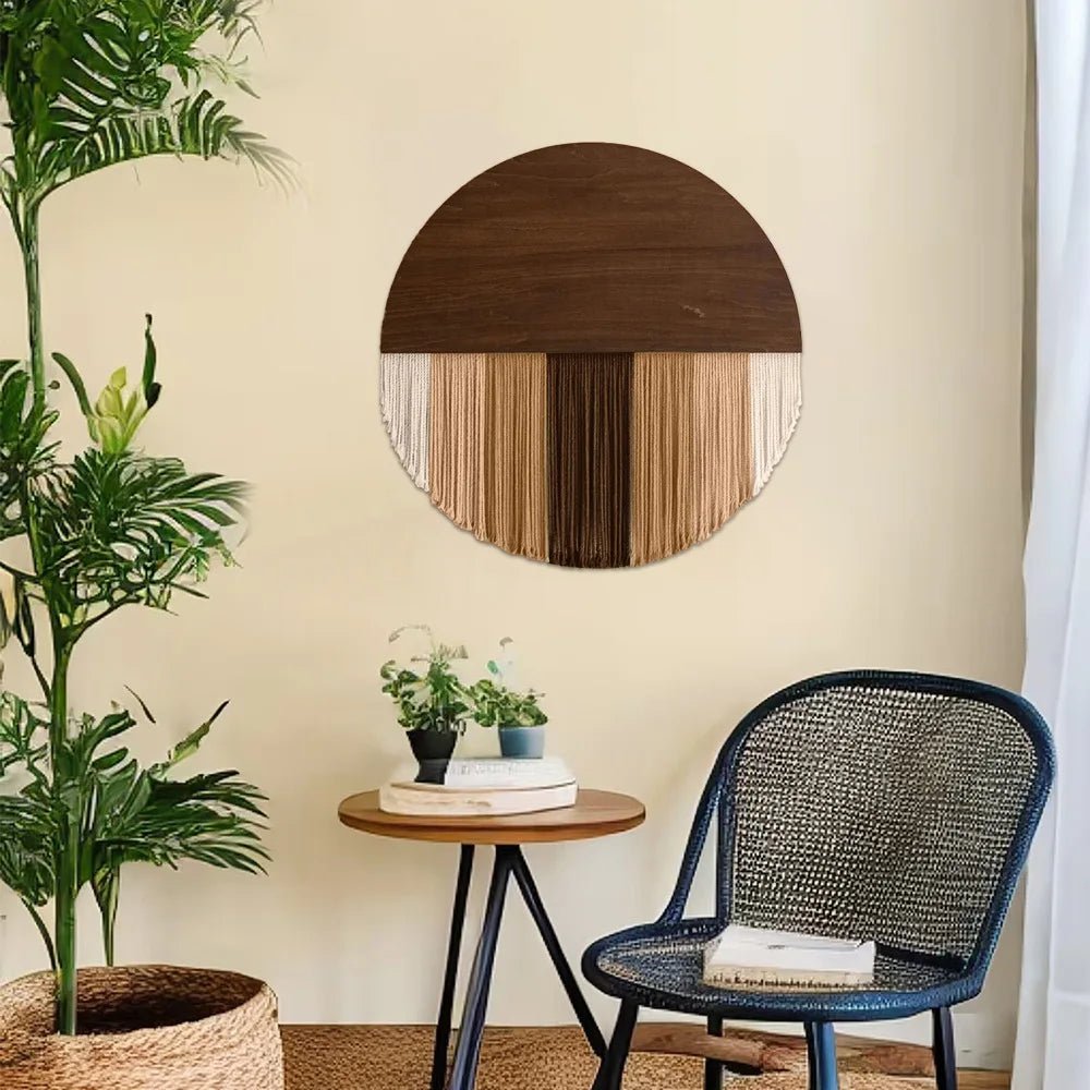 Image d'une décoration murale en macramé suspendue au-dessus d'une petite table ronde en bois avec des plantes. La pièce maîtresse circulaire combine un demi-disque en bois foncé avec des franges de cordes en coton de couleurs naturelles, créant un effet bohème chic. Un fauteuil en rotin noir et une plante verte en pot complètent le décor intérieur minimaliste et chaleureux.
