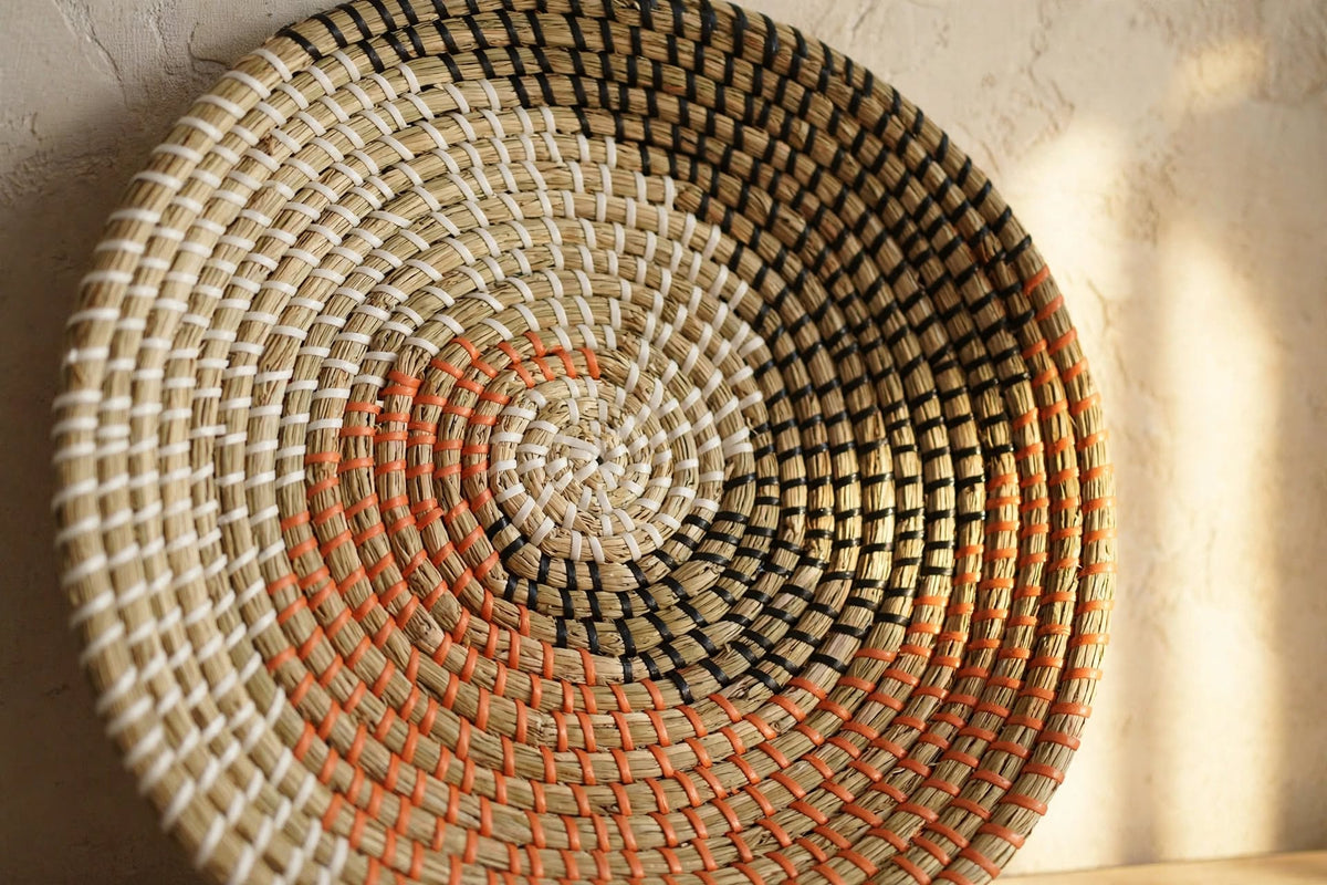 Gros plan sur un plat tressé en spirale écru, noir et orange saumon