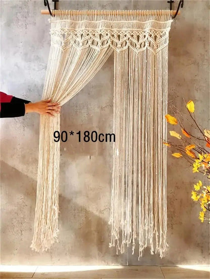 Un Élégance Bohème en  macramé rideau ivoire est suspendu à une tringle en bois clair.
Une main tenant le rideau révèle une ouverture partielle sur un fond de mur texturé gris.
Les dimensions "90 * 180cm" sont affichées en superposition sur le rideau.
Des éléments de décoration végétale avec des fleurs jaunes sont visibles sur le côté droit.