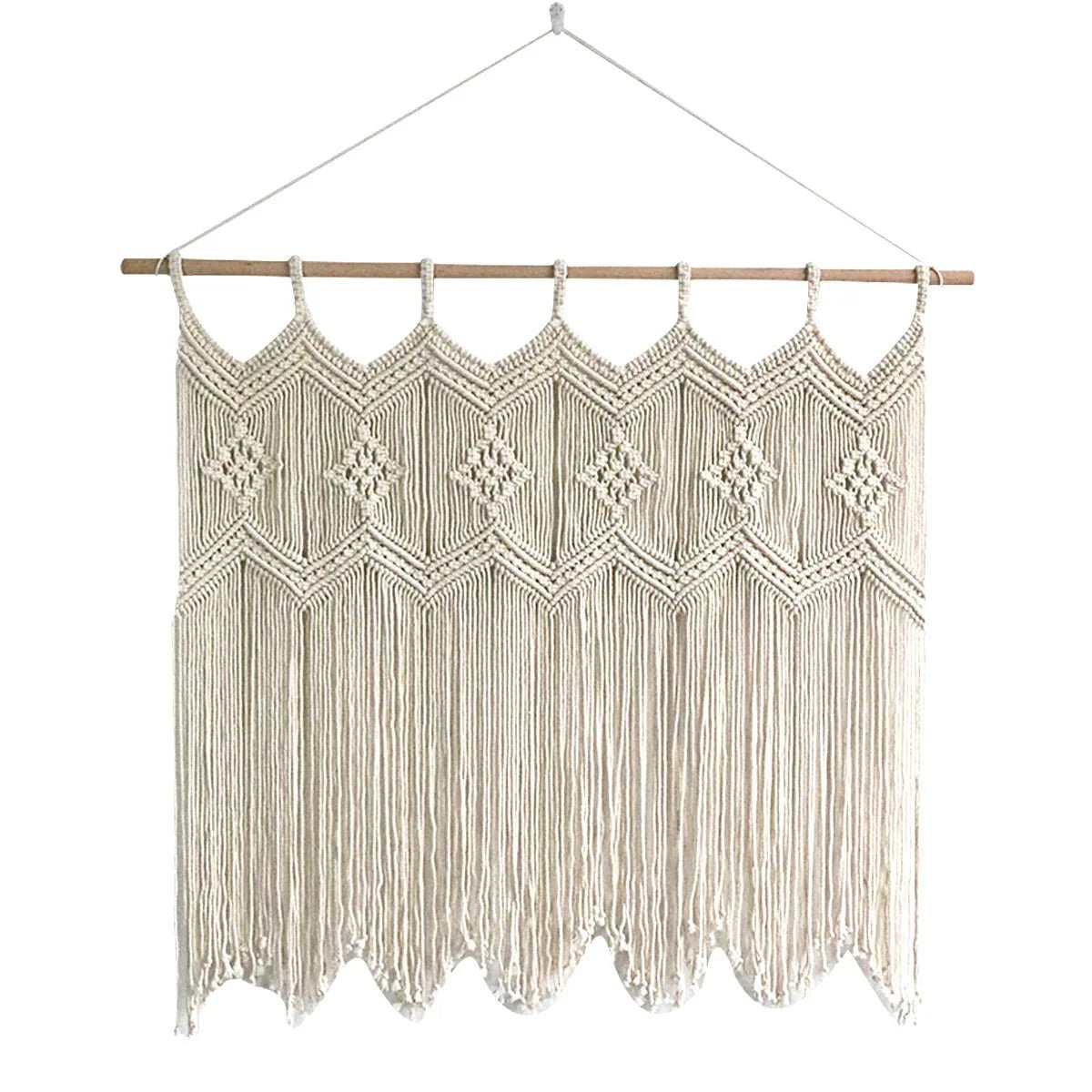 Un rideau en macramé de couleur crème, suspendu par une corde à une tringle en bois clair, est centré sur un fond blanc. Le motif complexe du macramé comprend des losanges centraux et des détails noués sur toute la surface. Le bas du rideau présente une bordure festonnée de franges tombantes.