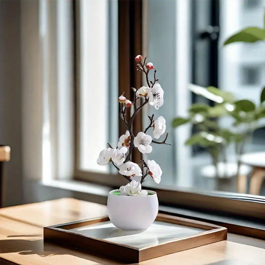Plante artificielle fleurie et élégante, posée sur une table en bois près d'une fenêtre.