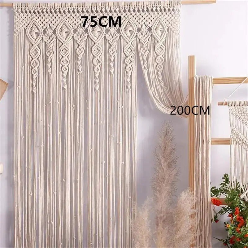 macramé rideau de couleur crème suspendu à une tringle en bois.
Le rideau mesure 75 cm de large et 200 cm de long.
Il présente un motif décoratif complexe dans la partie supérieure et de longues franges droites sur le reste de sa longueur.
Le rideau laisse apparaître partiellement un mur clair et quelques éléments de décoration intérieure flous.