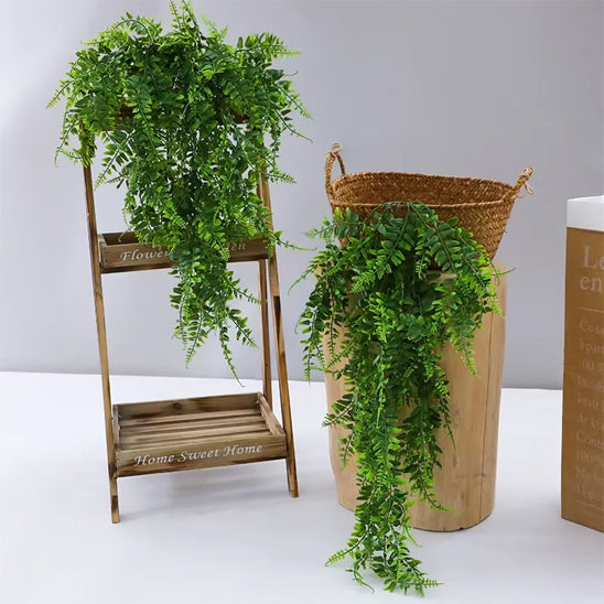  deux magnifiques plantes artificielles retombantes avec des feuilles vertes luxuriantes.
L'une est délicatement posée sur une étagère en bois à deux niveaux, ajoutant une touche de verdure suspendue.
L'autre cascade d'un panier en osier placé sur un support cylindrique en bois clair.
Ces plantes artificielles retombantes apportent une ambiance naturelle et décorative sans nécessiter d'entretien.
L'ensemble crée une scène intérieure chaleureuse et accueillante.