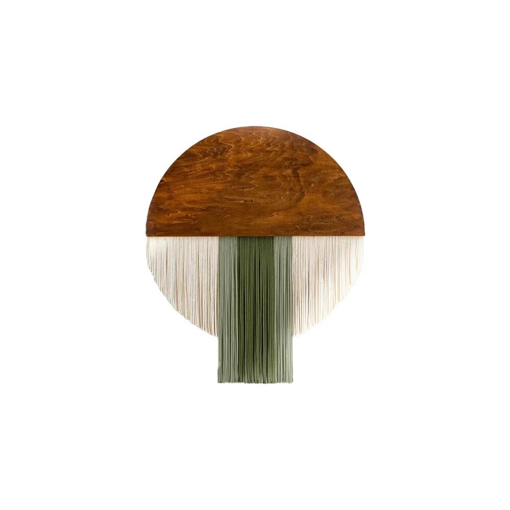 une décoration murale en macramé présentant une partie supérieure en bois de forme semi-circulaire de couleur marron. Des franges de cordes en coton de couleurs ivoire et vert olive pendent de la partie en bois. Les dimensions indiquées sont de 40 cm de largeur et 50 cm de hauteur.