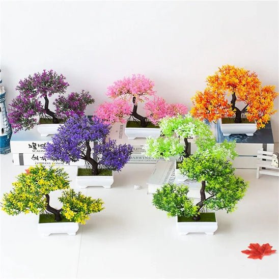 La photo présente un assortiment de petites plantes artificielles disposées sur une surface blanche. Ces plantes artificielles imitent des bonsaïs avec des feuillages de différentes couleurs vives : violet, rose, orange, vert clair et vert foncé. Chaque plante artificielle est placée dans un petit pot carré blanc. L'ensemble crée une décoration colorée et sans entretien grâce à ces plantes artificielles.