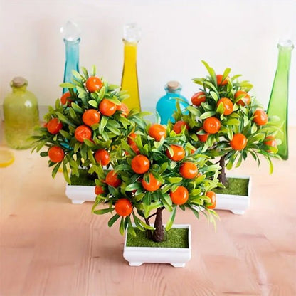 Sur une table en bois clair, on aperçoit trois petits pots blancs contenant chacun une plante artificielle imitant un agrume. Ces plantes artificielles sont dotées de feuilles vertes et de petites oranges vives. À l'arrière-plan, plusieurs bouteilles décoratives en verre coloré ajoutent une touche vive à la scène. L'ensemble crée une ambiance fraîche et artificielle.