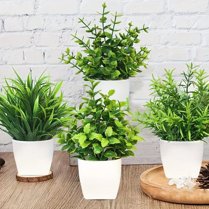 Quatre mini-plantes artificielles aux feuilles vertes luxuriantes sont disposées dans des pots blancs sur une surface en bois, adossée à un mur de briques blanches, pour une décoration intérieure chic et sans entretien. Un plateau en bois orné d'éléments décoratifs est visible.