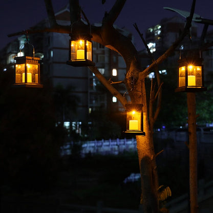 Quatre lanternes solaires de jardin haut de gamme Classic-Solar™ brillent la nuit dans les branches des arbres, illuminant l'obscurité avec un design rétro. Les arbres et les appartements à proximité contribuent à l'ambiance chaleureuse, idéale pour une lanterne solaire d'extérieur.
